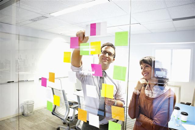 Man and women sticking post-it notes to glass